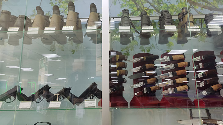 Вид на витрину с пневматическими пистолетами, биноклями и ножами в магазине Хищник.