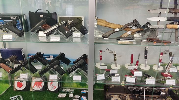 Вид на витрину с пневматическими пистолетами и ножами в магазине Хищник.